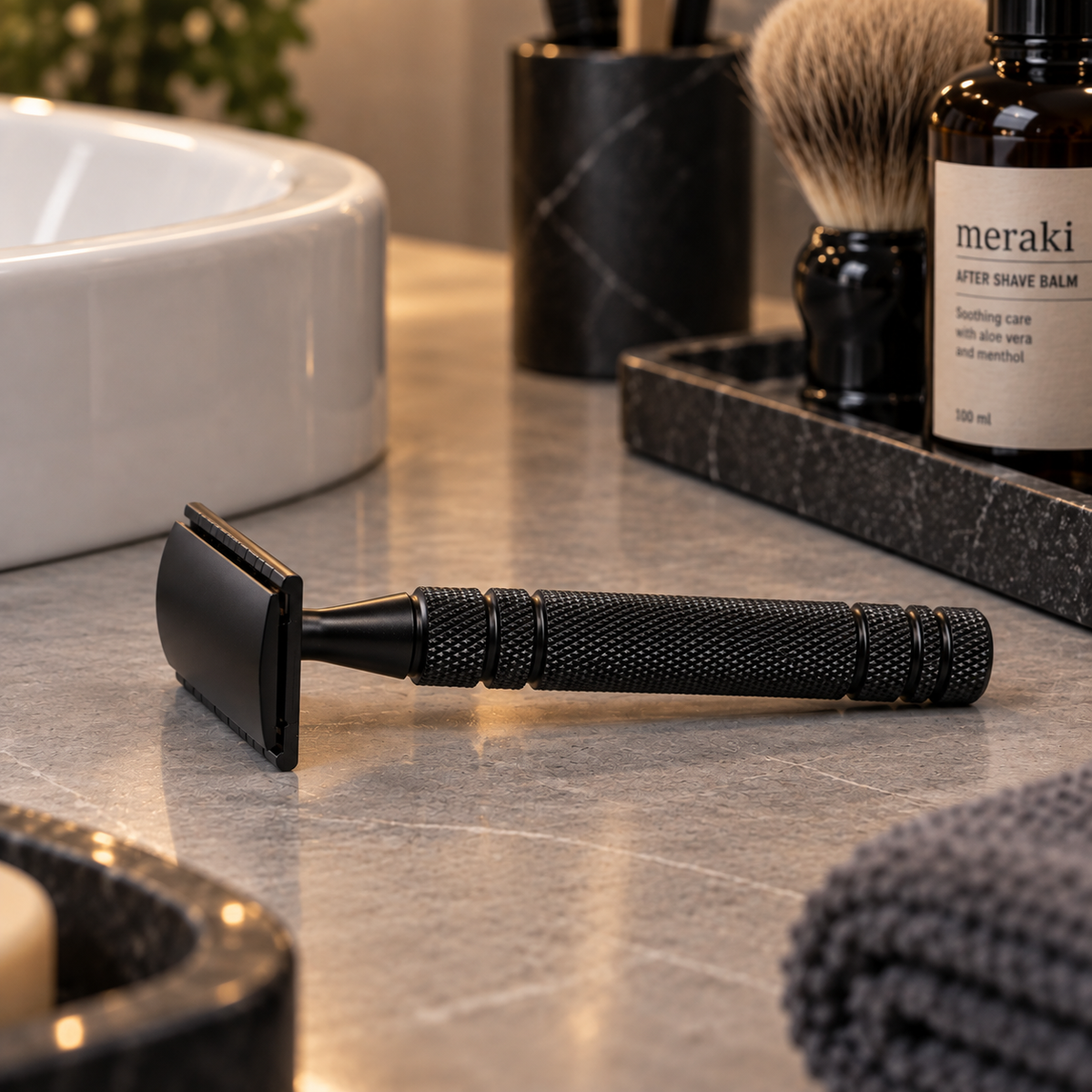 Klassisk barberhøvel i matt svart med strukturert håndtak på baderomsbenken sammen med barberkost og aftershave