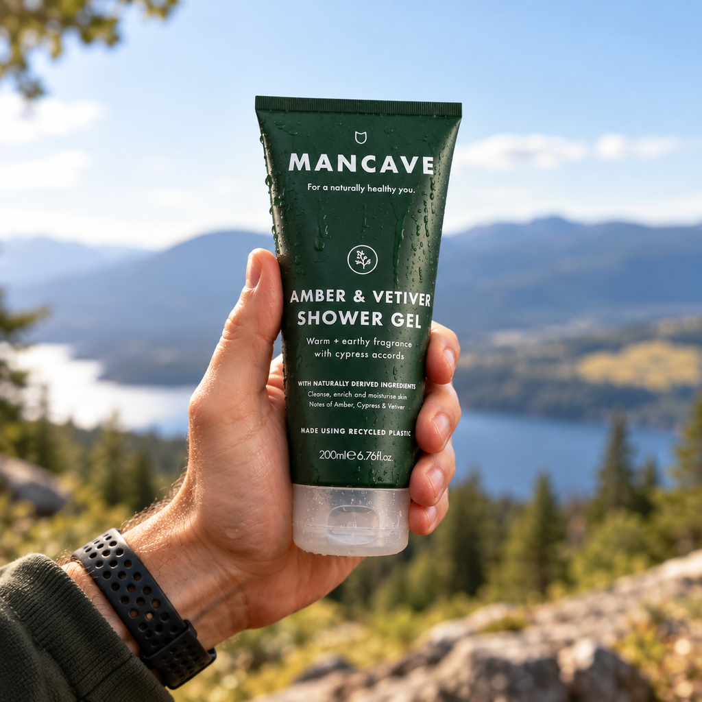 ManCave Amber & Vetiver Shower Gel holdes i hånden utendørs med fjell og natur i bakgrunnen